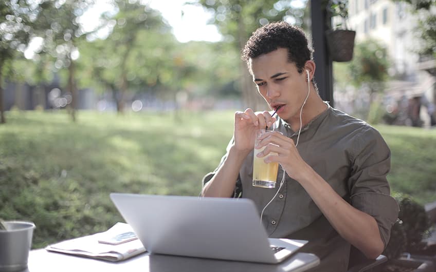 Black Man sipping lemonade while working on his laptop computer outdoors at a park